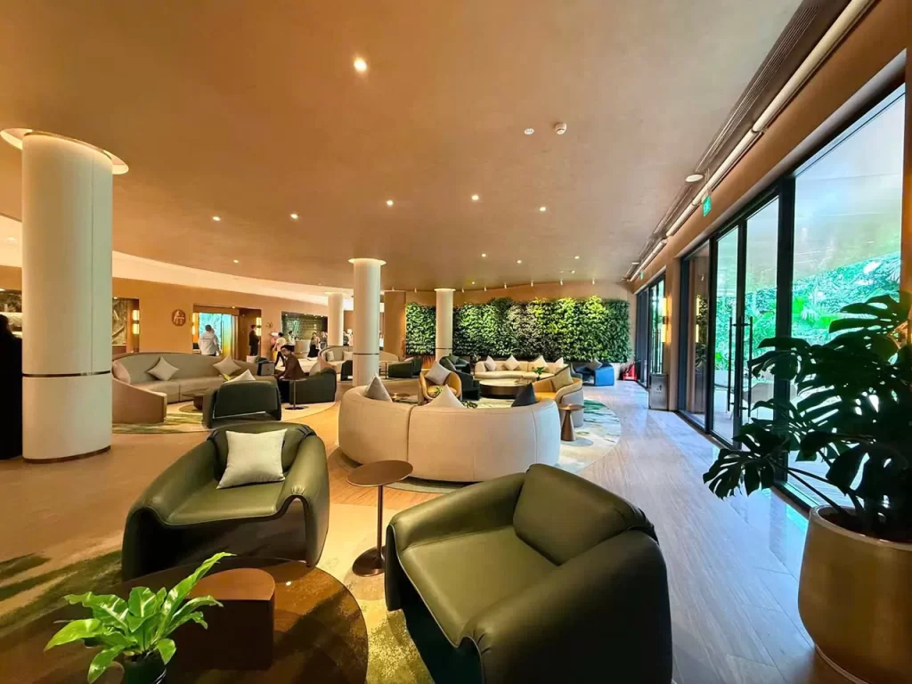 Sảnh lounge nhà mẫu Palm River với tường cây và cửa kính nhìn ra vườn